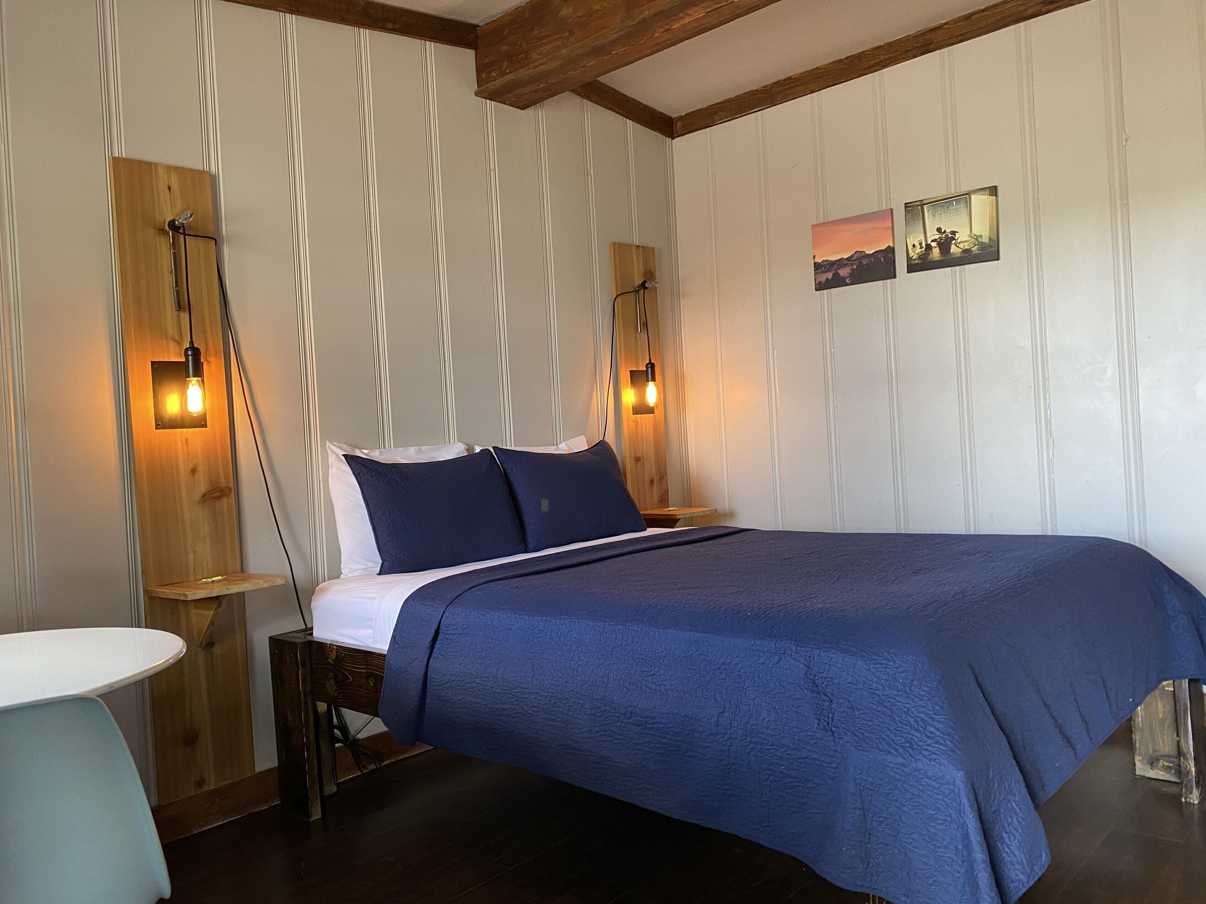 A bedroom with a large bed, wooden headboard, two bedside tables, and wall-mounted lights.