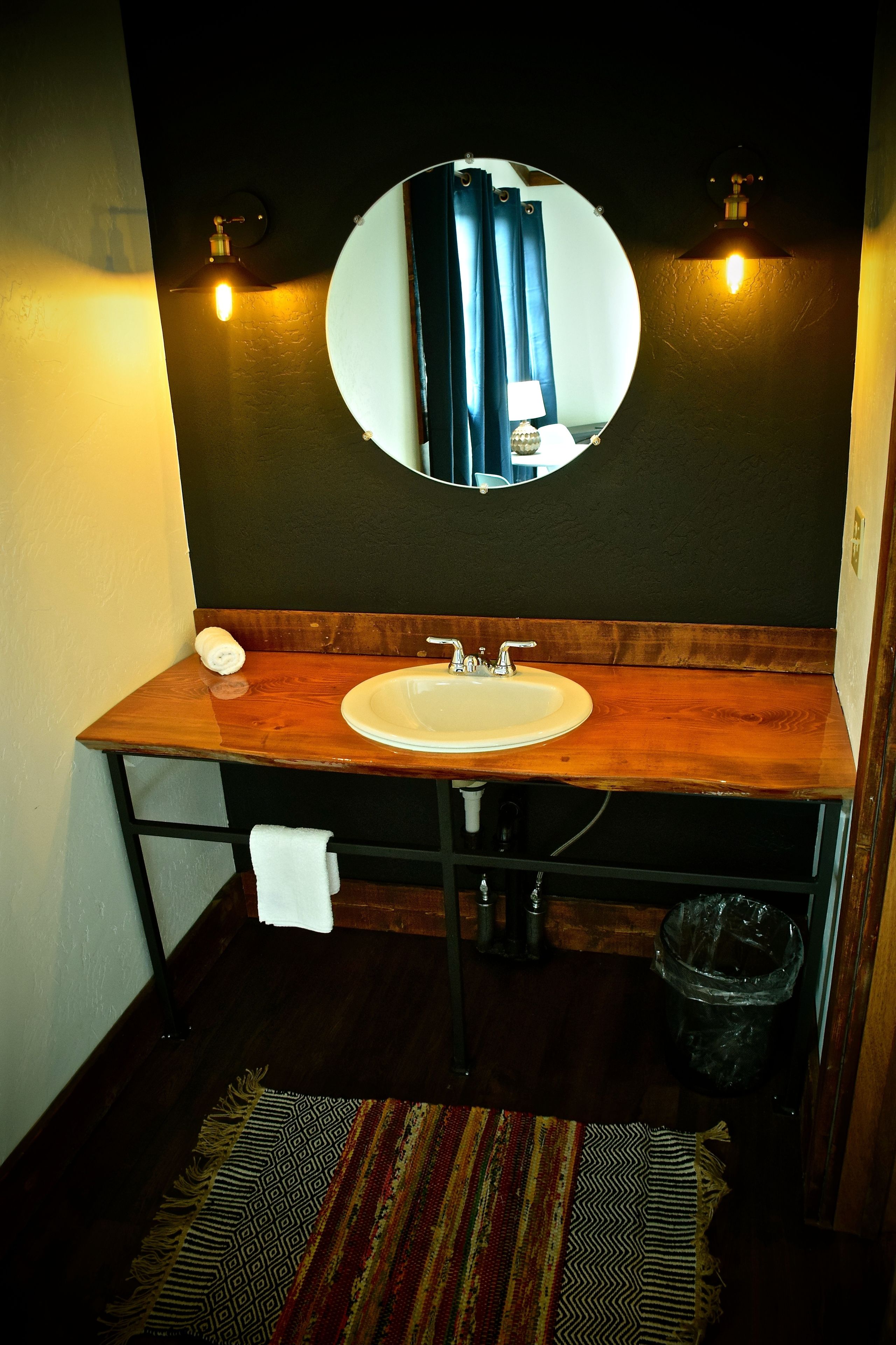 A bathroom with a wooden vanity, a round mirror, and a white sink.