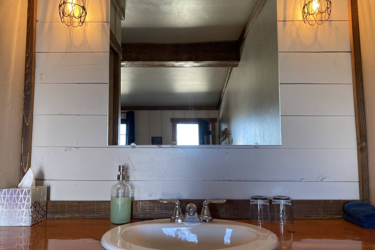 A bathroom with a large mirror, wooden panel walls, a white sink, and two wall-mounted lights.