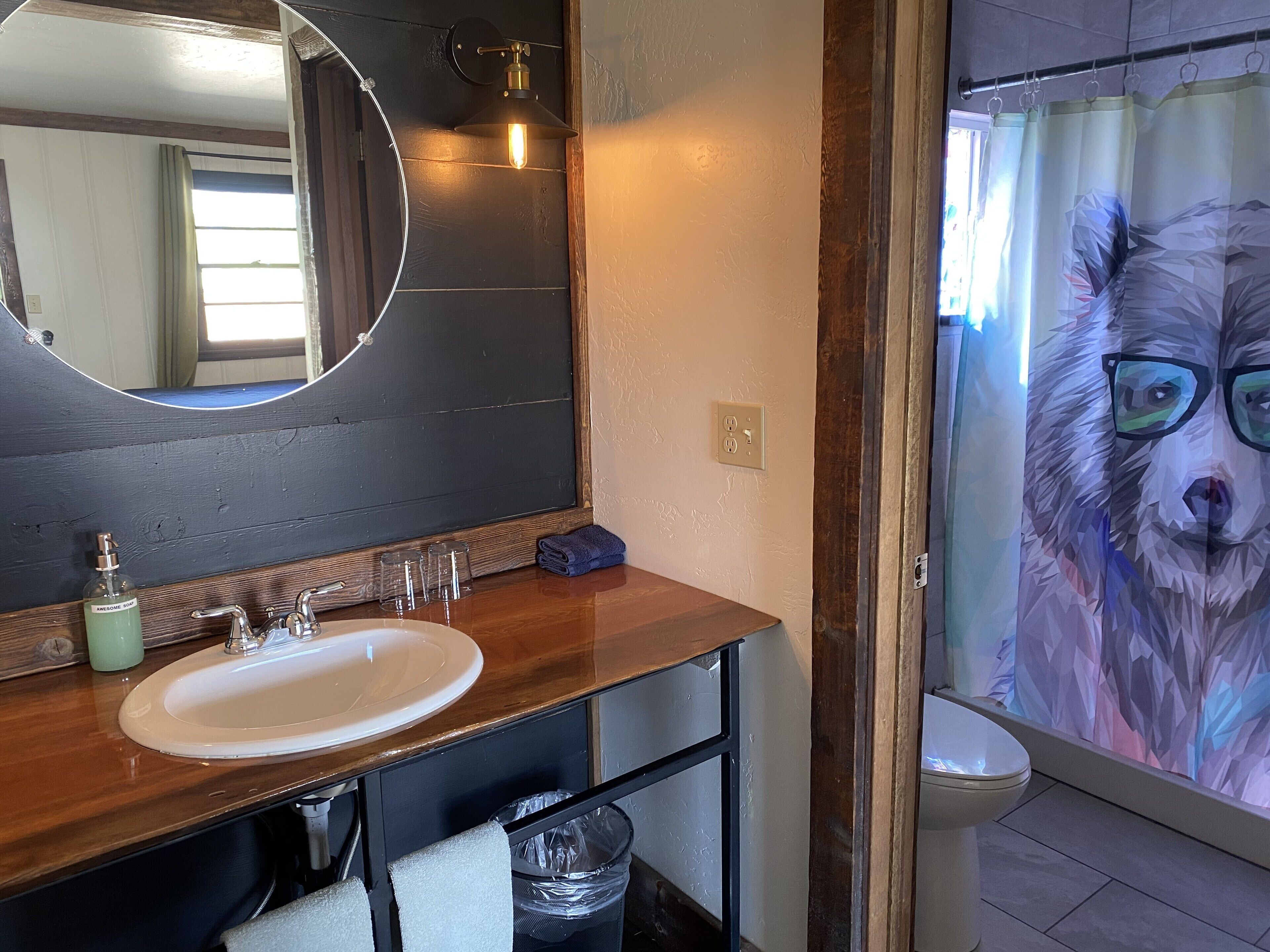 A bathroom with a wooden vanity, a round mirror, a white sink, and a shower curtain with a geometric animal design.