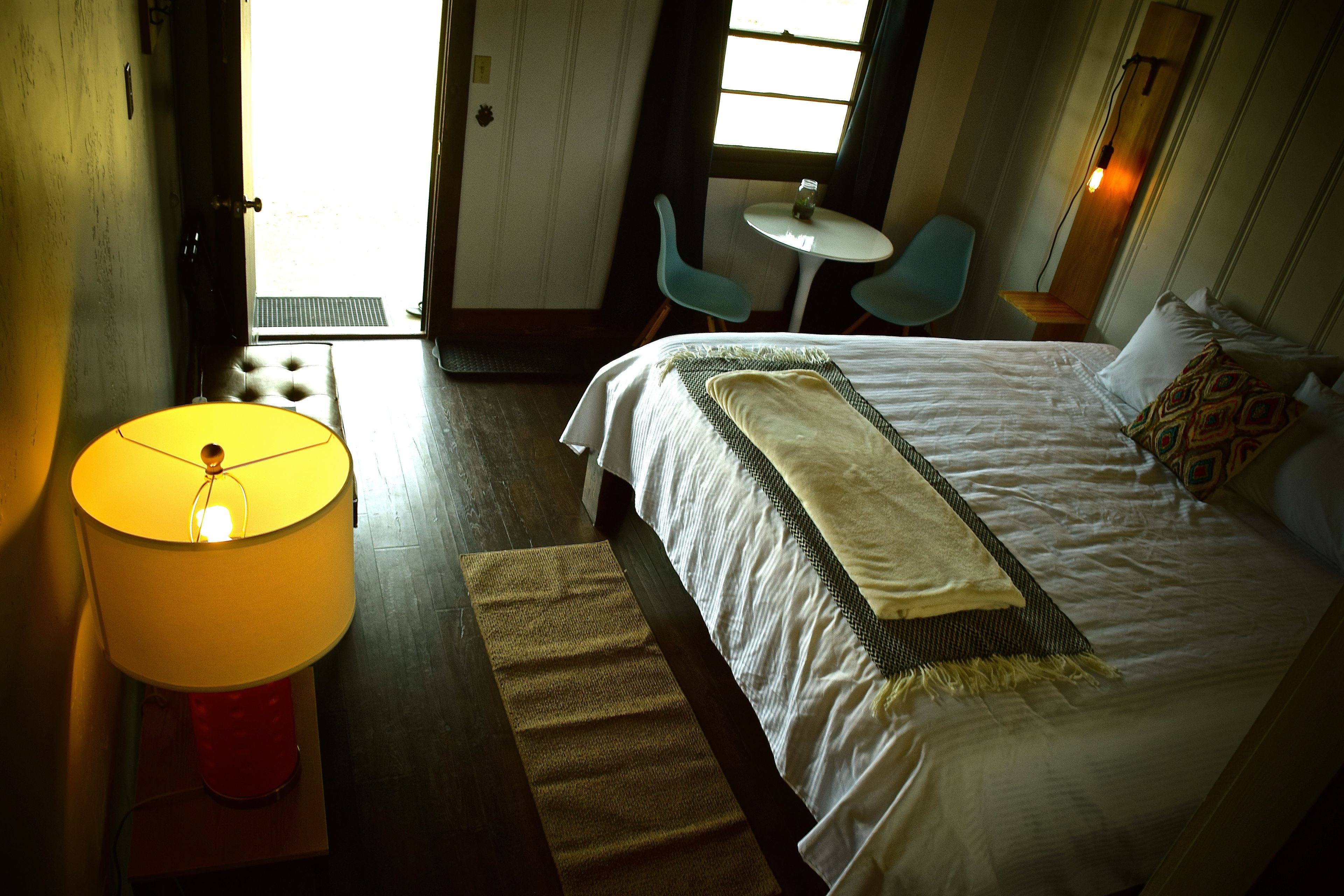 Une chambre d’hôtel avec un lit, une table, deux chaises et une lampe.