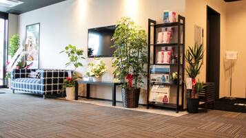 A modern lobby with a patterned carpet, a sofa, a TV mounted on the wall, and a bookshelf with potted plants.
