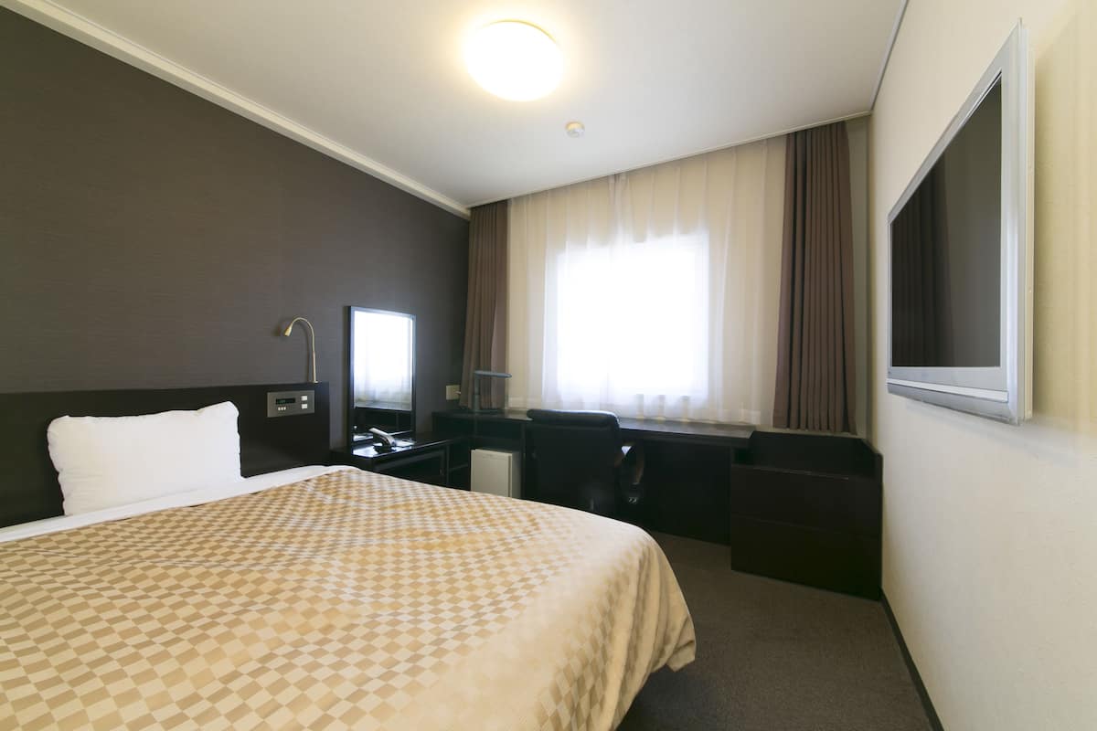 Une chambre d’hôtel avec un lit, un bureau, une chaise et une fenêtre avec des rideaux.