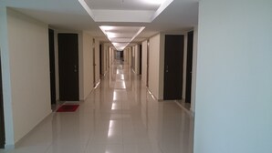 Un long couloir étroit, avec des portes de chaque côté, un tapis rouge à l’entrée et un sol carrelé brillant.