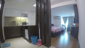 Une chambre d’hôtel de taille réduite, équipée d’une kitchenette, d’un lit, d’un bureau et d’une salle de bain.