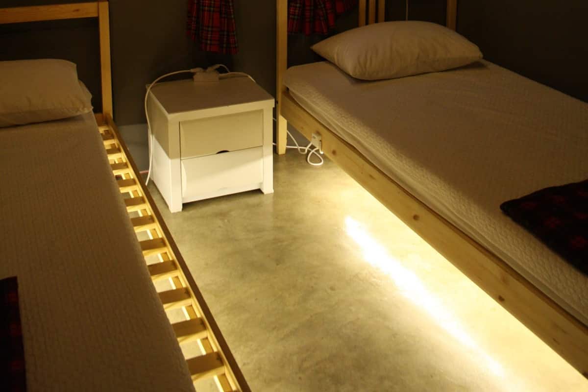 A small room with two beds, a nightstand, a window with plaid curtains, and a ceiling light.