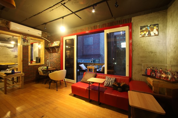 A cozy living room with a red sofa, wooden tables, and a brick wall.