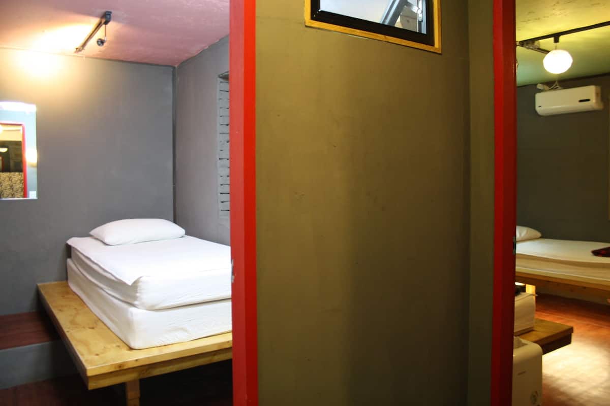 A single bed with a wooden headboard in a room with a red accent wall and a small window.