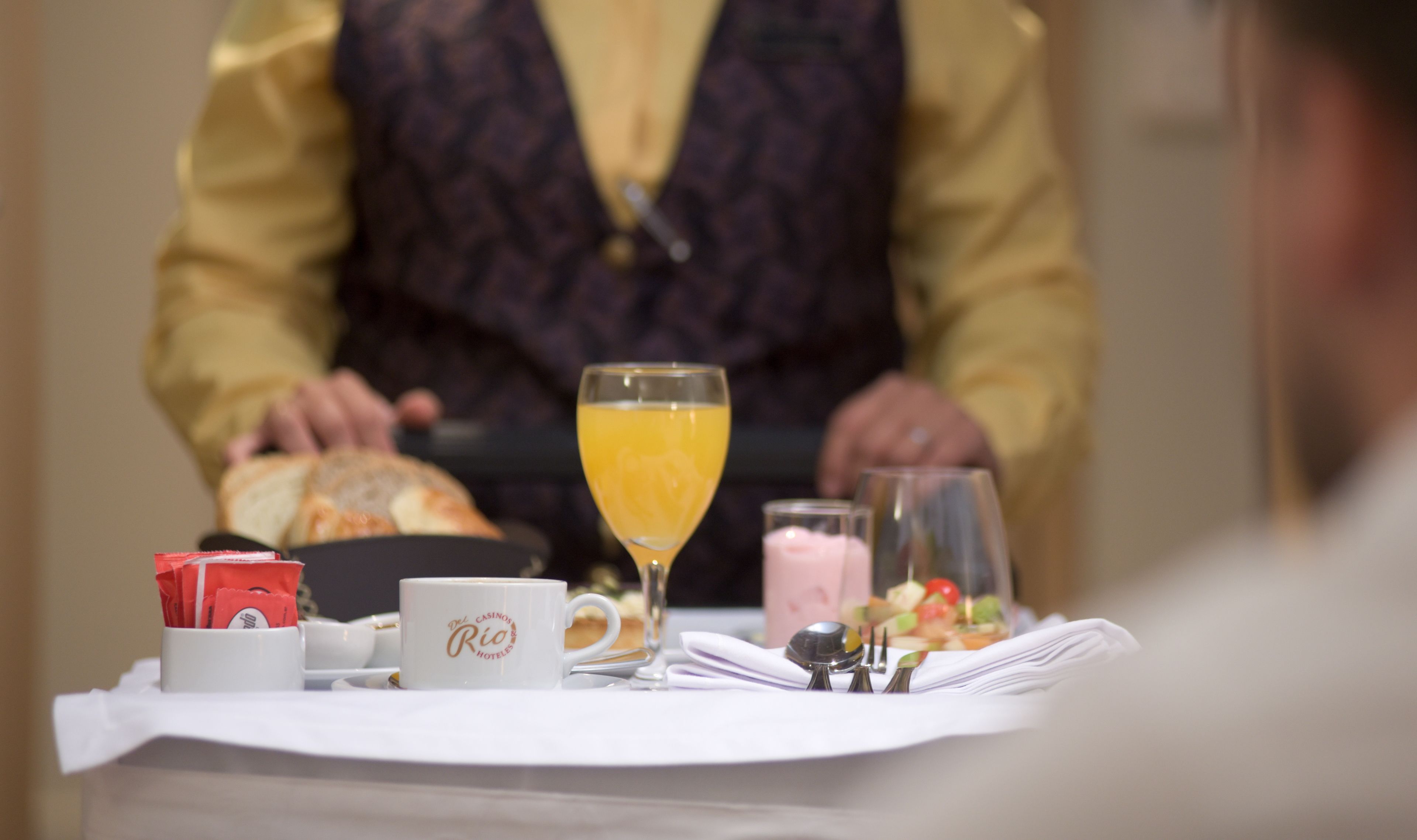 Un desayuno con un croissant, un vaso de jugo de naranja, una taza con la etiqueta 'Del Rio' y un plato pequeño de fruta.