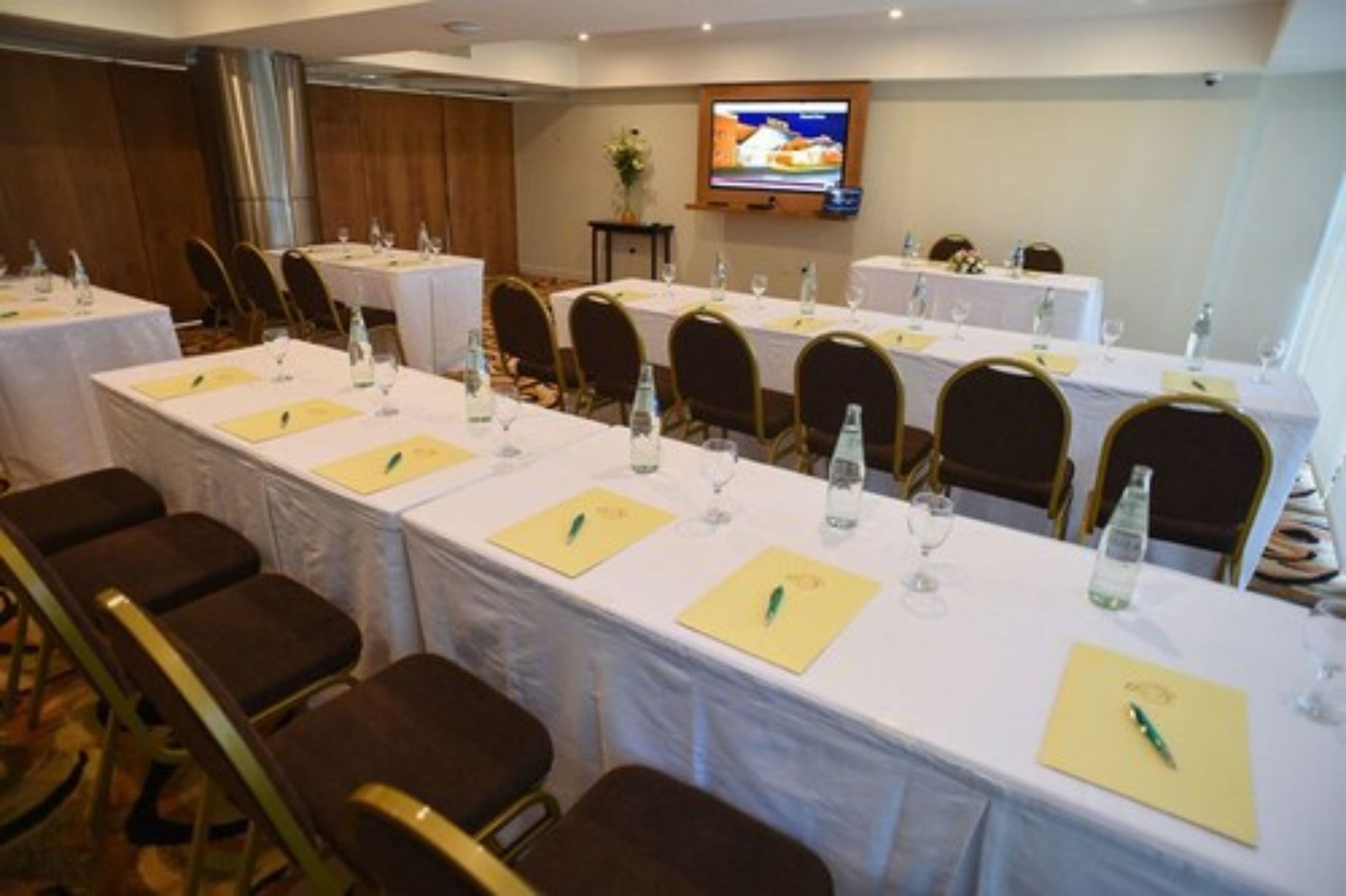 A conference room with long tables, chairs, and a television screen.