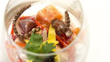 A clear glass bowl containing a seafood salad with octopus, red bell peppers, and a garnish of parsley.