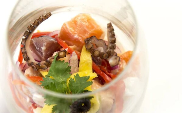 Un bol de vidrio transparente con una ensalada de mariscos que incluye pulpo, pimientos rojos y una guarnición de perejil.