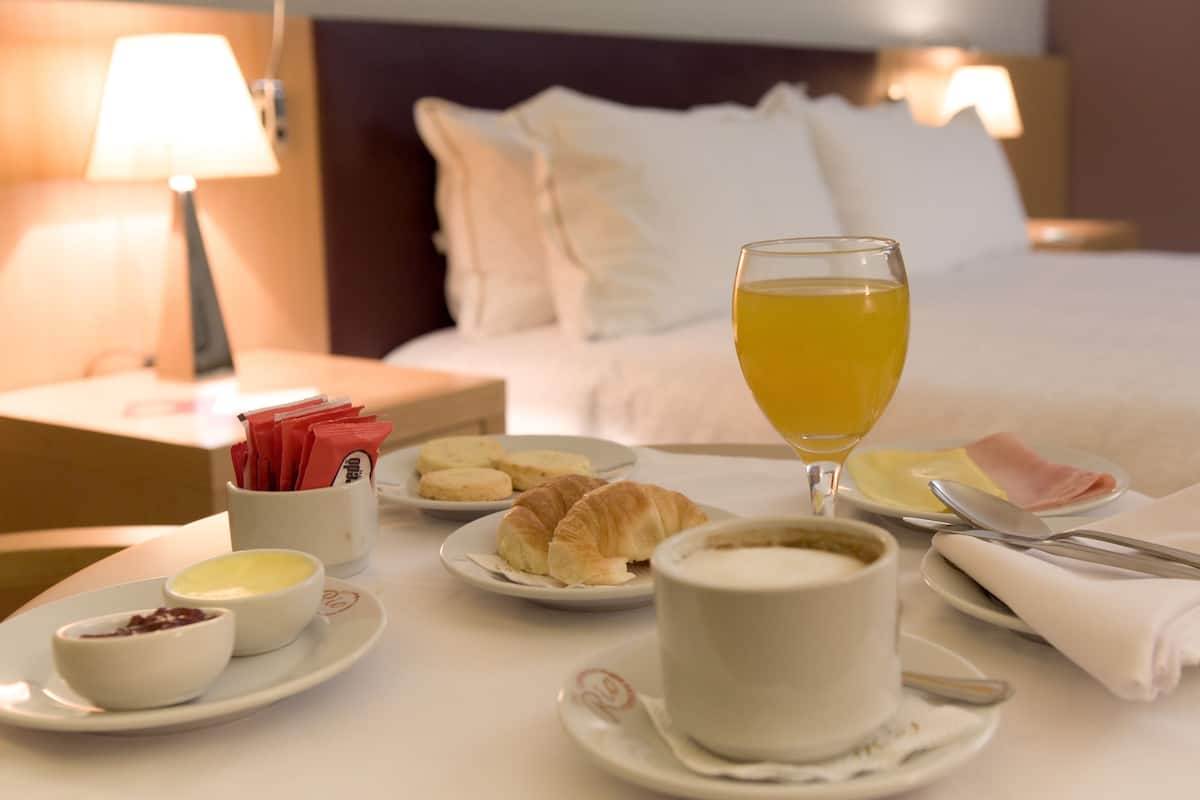 En frukostuppsättning med croissanter, ett glas apelsinjuice och små skålar med sylt och smör, placerat på ett bord i ett hotellrum.