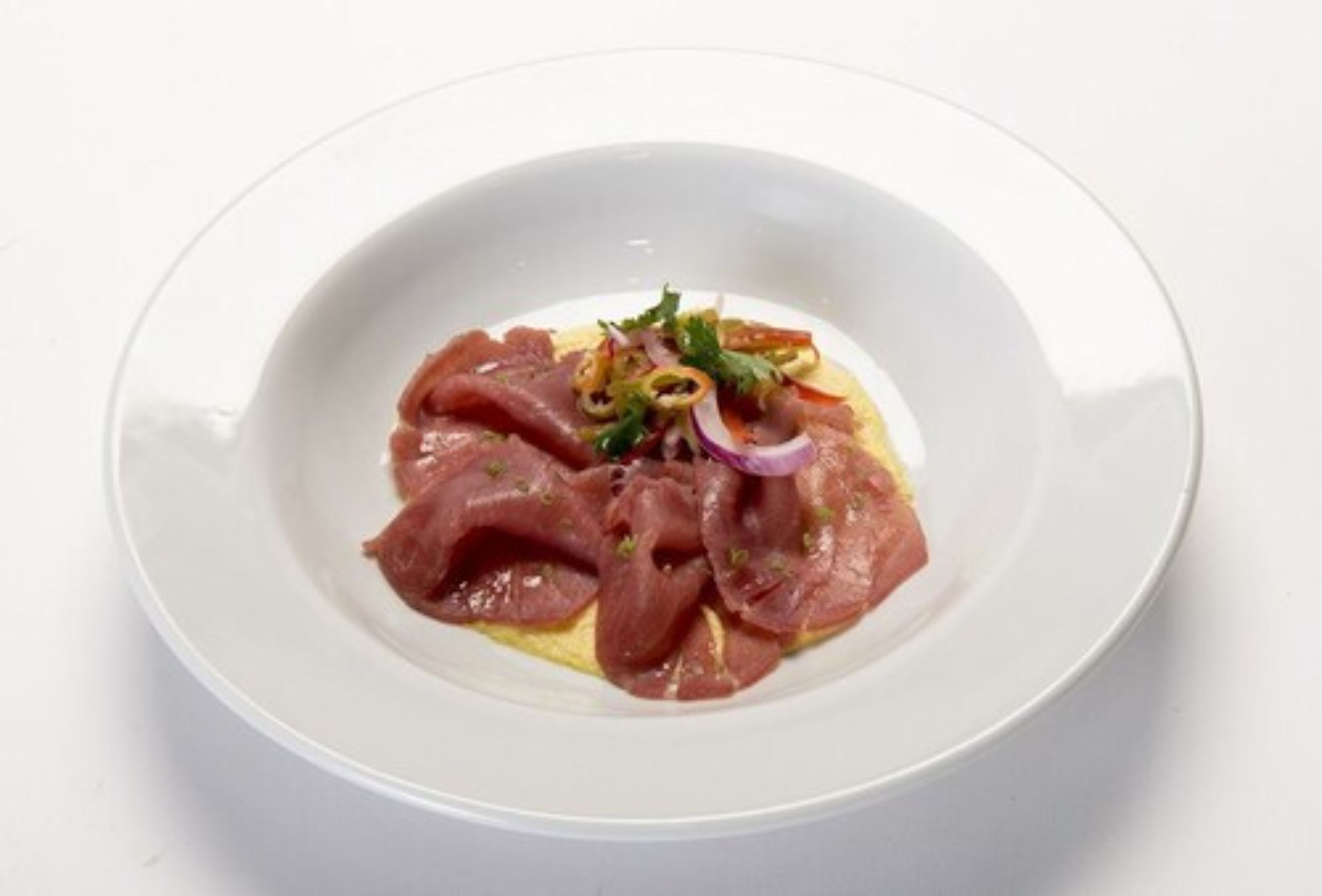 A white plate with thinly sliced meat, possibly prosciutto, garnished with red onion and herbs.