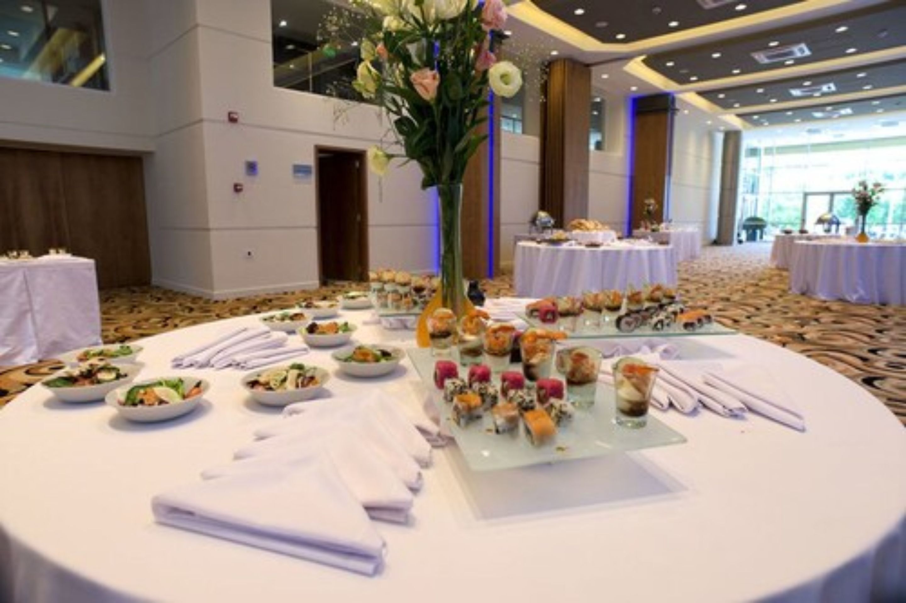 A banquet hall with round tables set for a meal, featuring various dishes and a centerpiece.