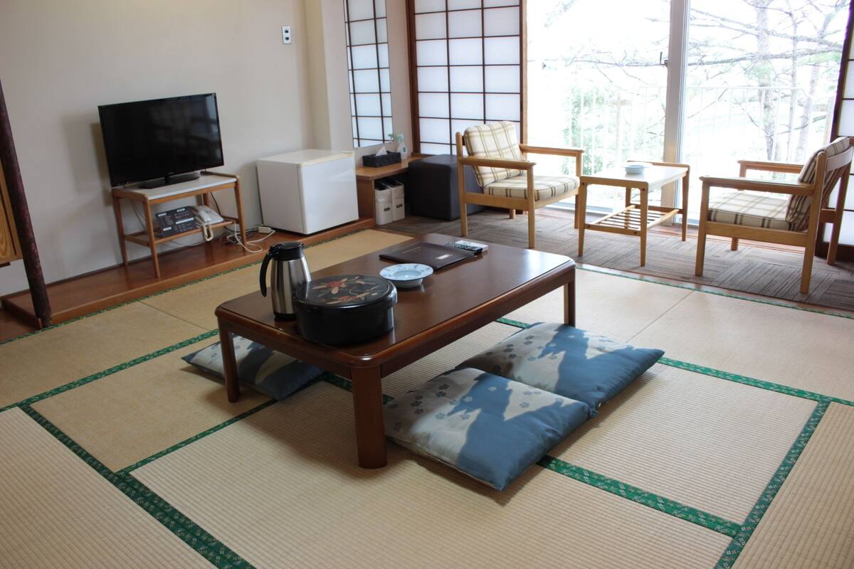 Un salón tradicional japonés con suelo de tatami, una mesa baja de madera y un televisor.