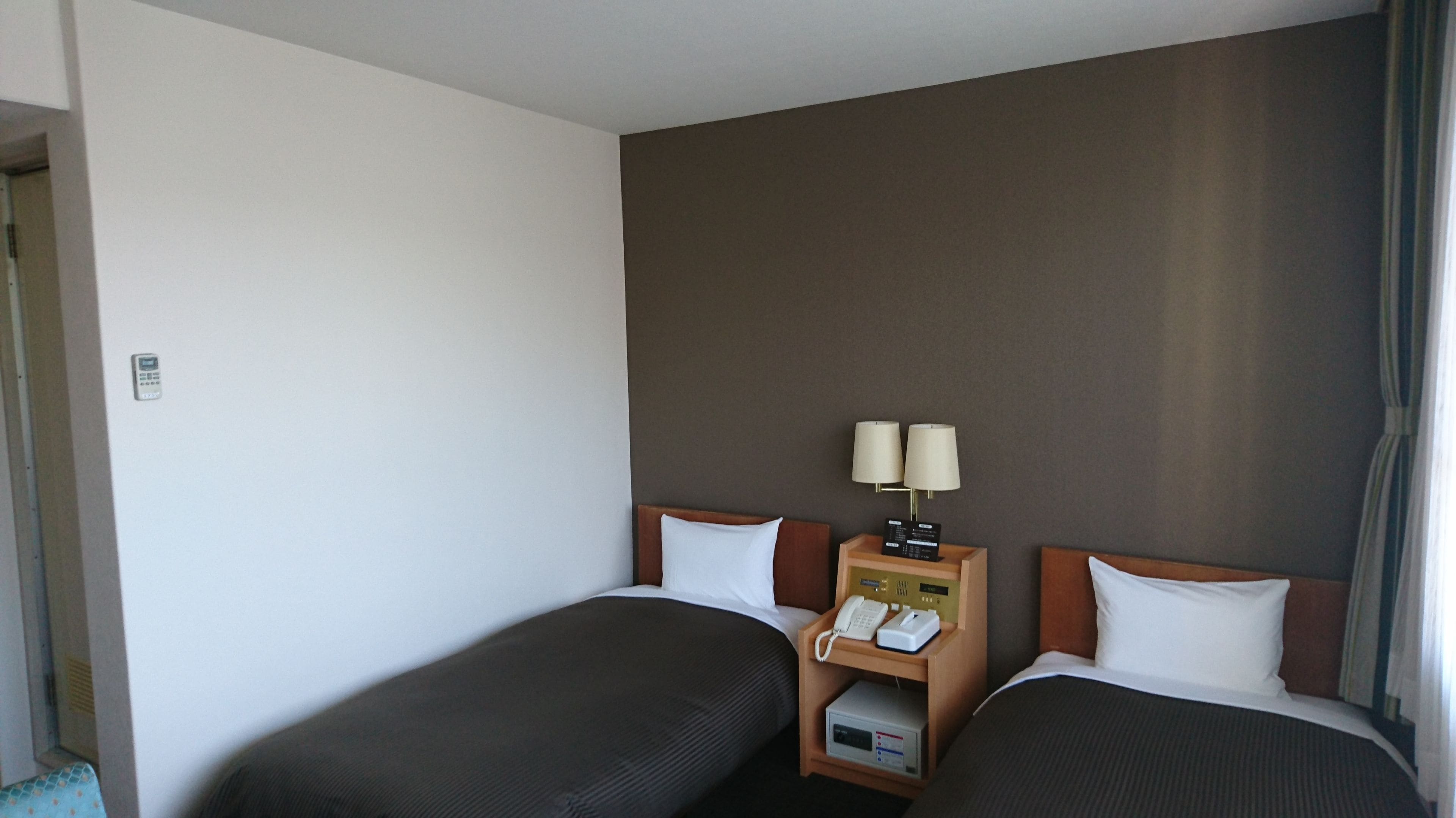 Et hotelværelse med to senge, et natbord med lampe, telefon og en lille hylde.