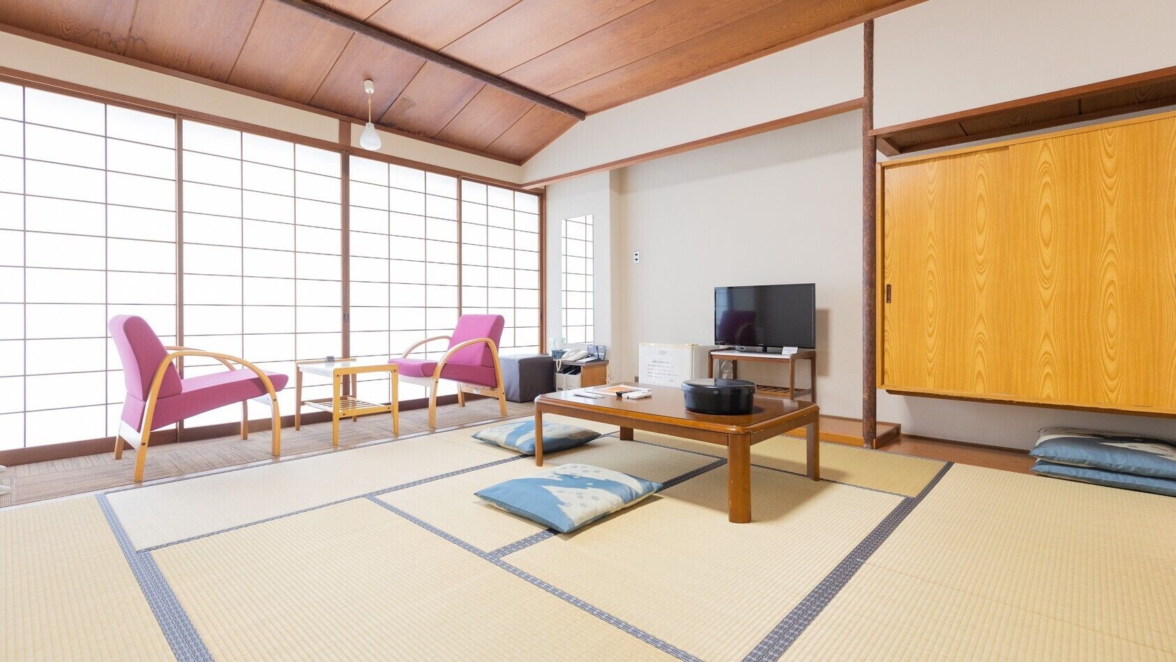 A traditional Japanese room with tatami flooring, a television, and a wooden wardrobe.