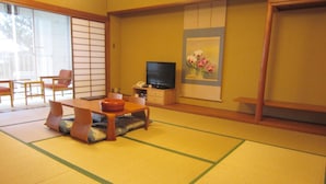 A traditional Japanese room with tatami flooring, a low table with cushions, a television, and a painting on the wall. - Hotel Axia Kushikino (Ichikikushikino)