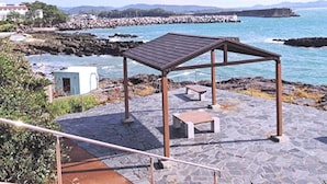 A stone-paved outdoor area with a wooden gazebo, a bench, and a small structure, overlooking a rocky coastline and a bridge. - Hotel Axia Kushikino (Ichikikushikino)