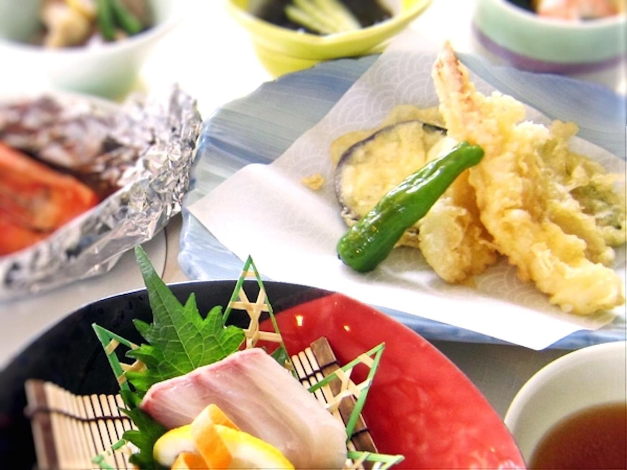 A variety of dishes including tempura, sashimi, and a bowl of soup.