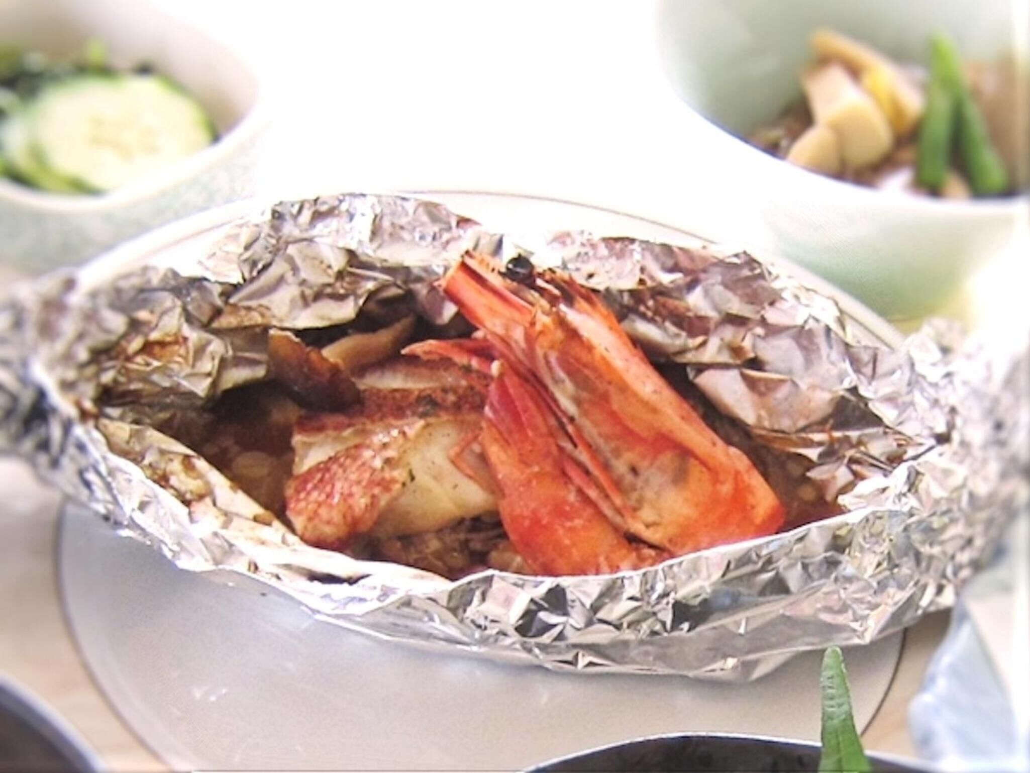 Un plato con un cangrejo envuelto en papel de aluminio, posiblemente cocido, y otros platos al fondo.