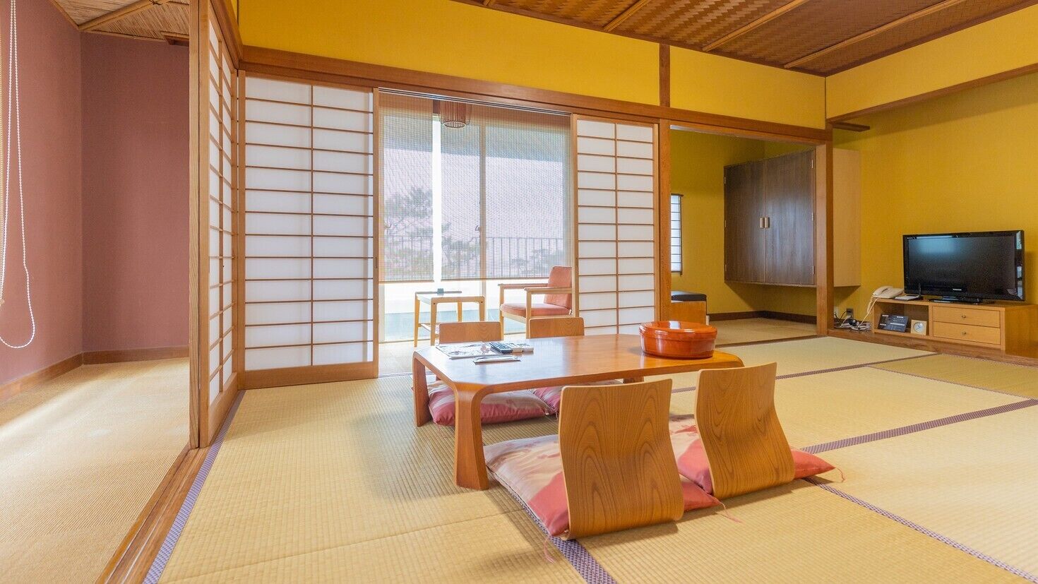 A traditional Japanese room with tatami flooring, a sliding door, a table with cushions, and a television.
