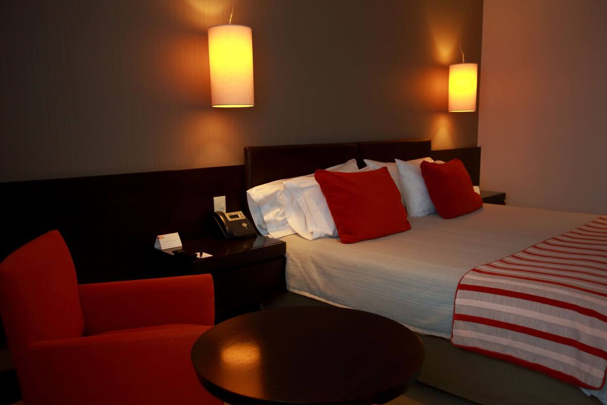 A hotel room with a bed, a nightstand, a phone, a chair, and two wall-mounted lamps.