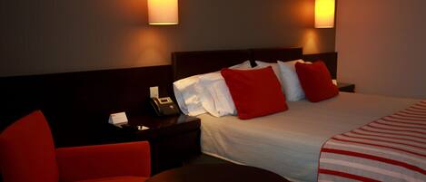 A hotel room with a bed, a nightstand, a phone, a chair, and two wall-mounted lamps.