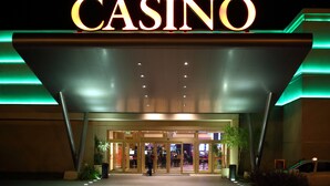 Entrada de un casino con señalización iluminada, acceso cubierto y el interior visible a través de puertas de vidrio.