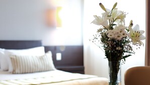 Una habitación de hotel con una cama, una mesita de noche y un jarrón con flores.