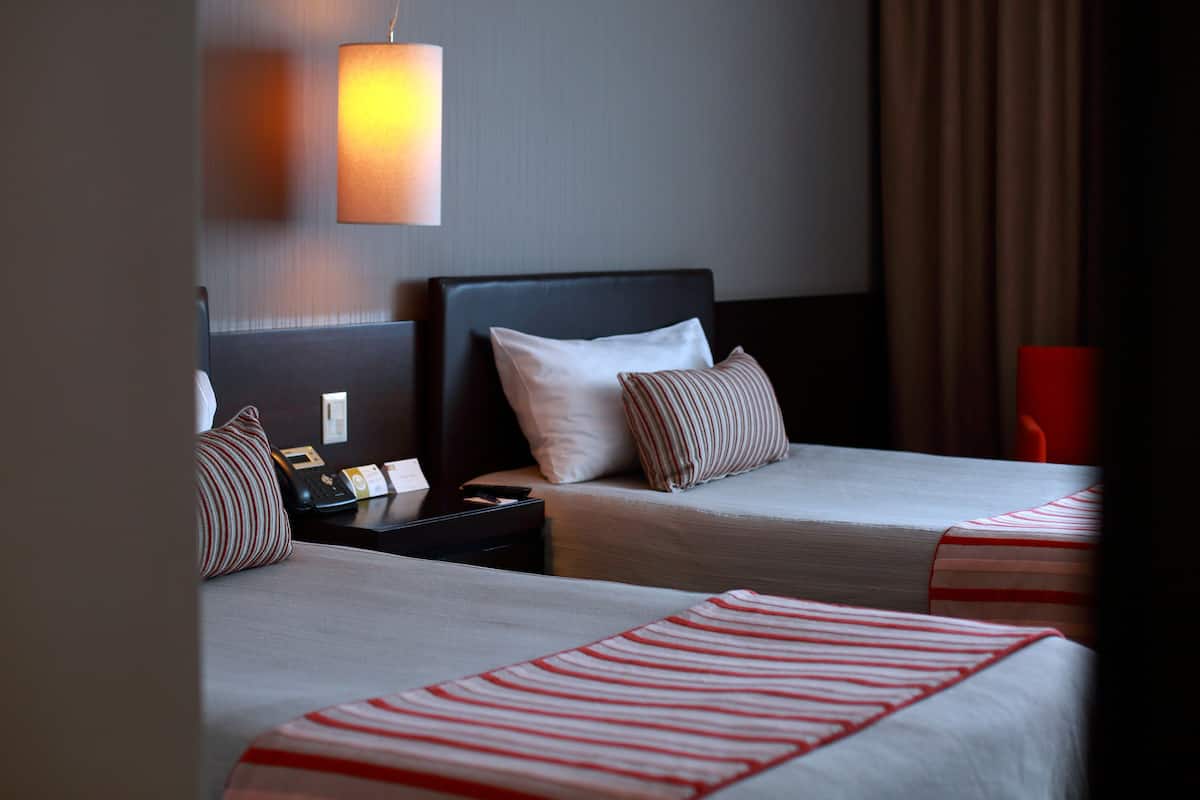 A hotel room with two beds, a nightstand, and a lamp.