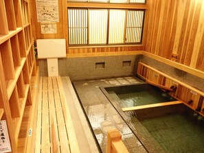 A traditional Japanese onsen with wooden interiors, a stone floor, and a small hot spring bath. - Gasthof Schi Heil (Nozawaonsen)