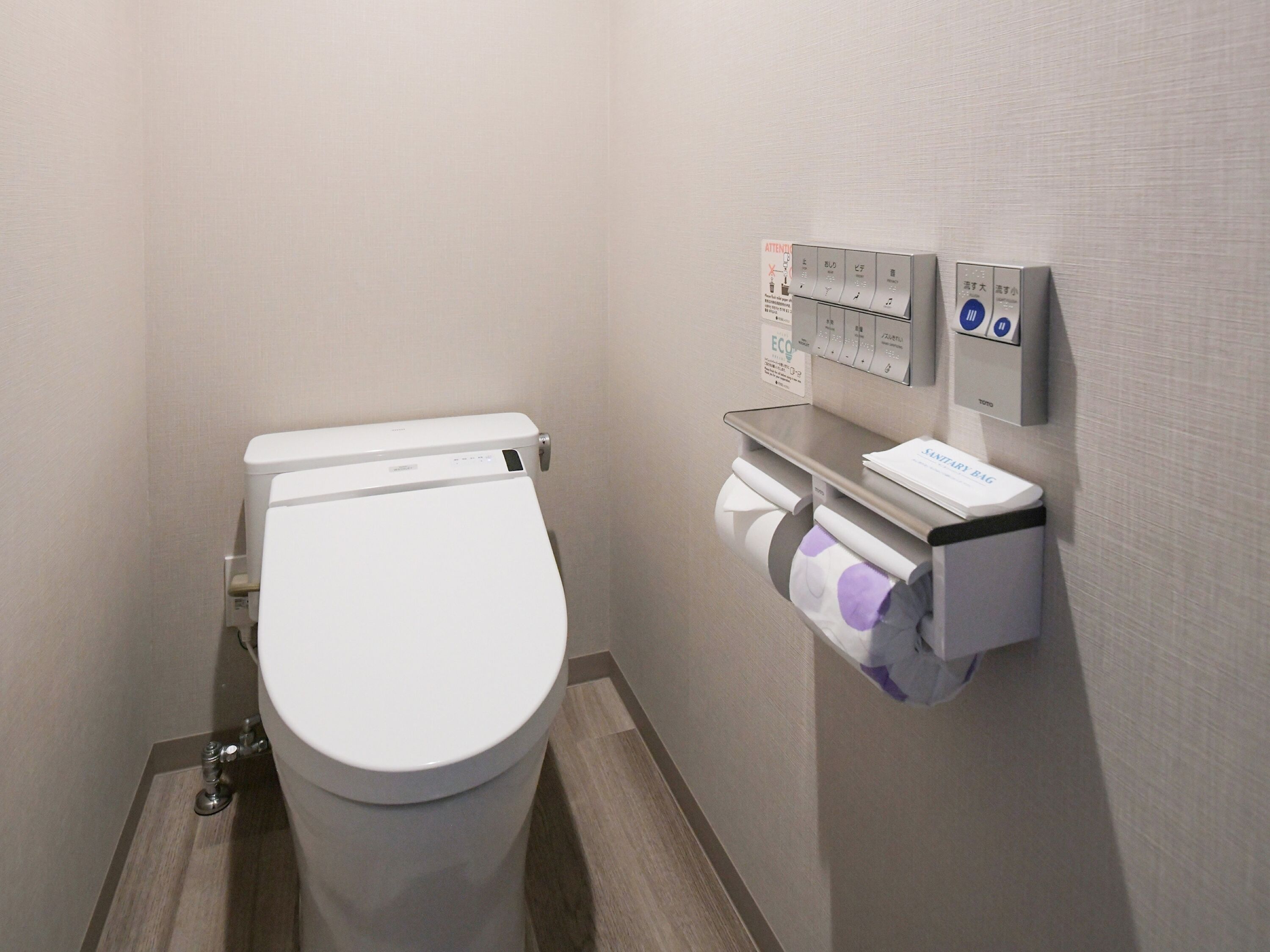 A modern bathroom with a white toilet, a paper towel dispenser, and a hand dryer.
