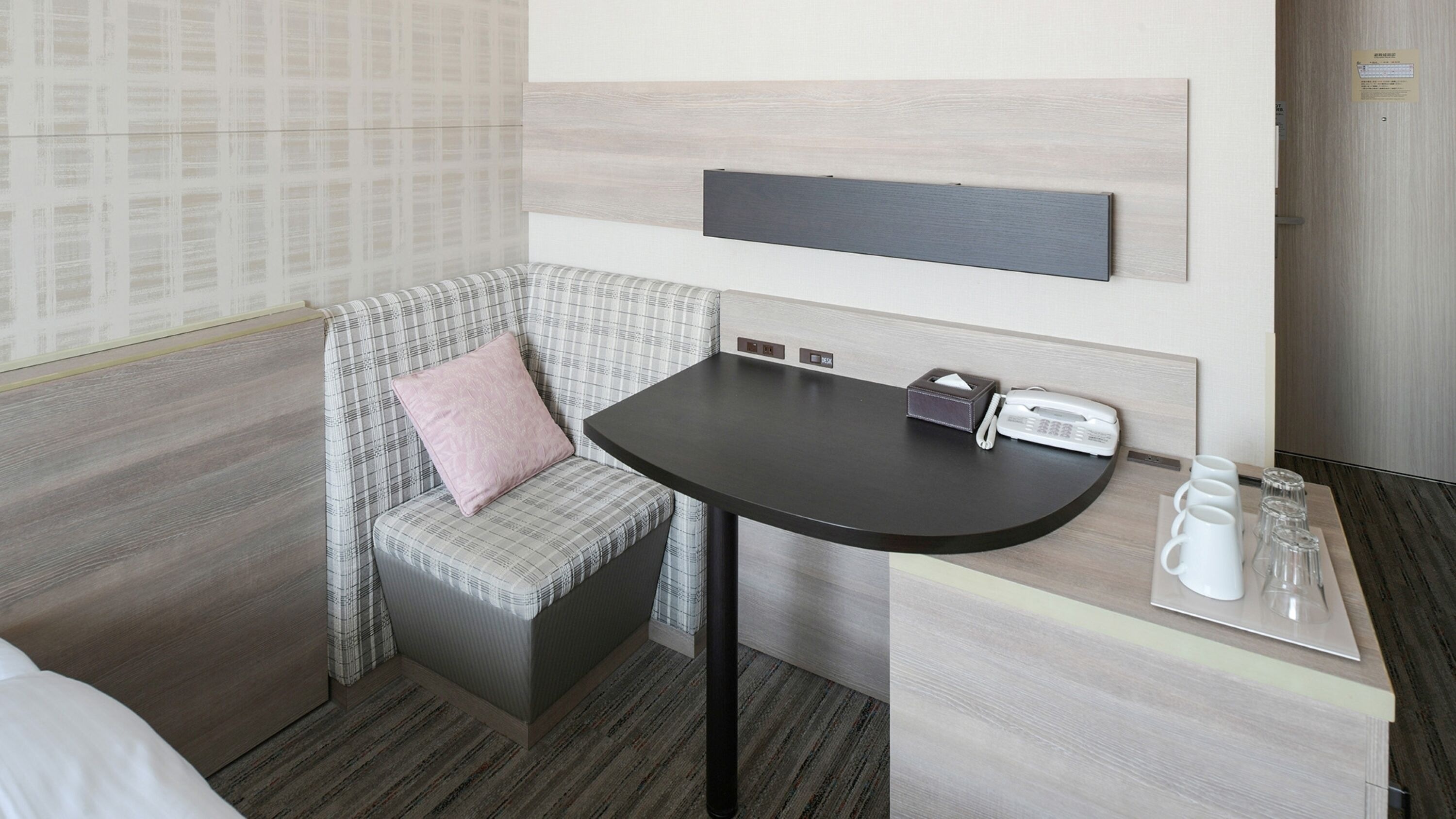 Ein kleines Hotelzimmer mit einer Sitzecke, einem Schreibtisch mit Telefon und Taschentuchbox sowie einer Kaffeestation.