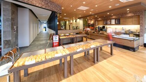 A bakery cafe with multiple display tables of baked goods, a coffee station, and a seating area with benches. - Vessel Inn Shiga Moriyama Station (Moriyama)