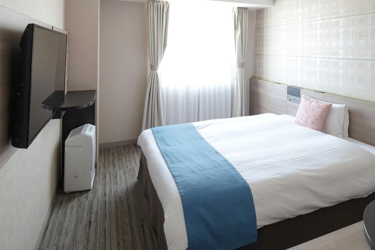 A hotel room with a bed, a TV, a desk, and a window with curtains.