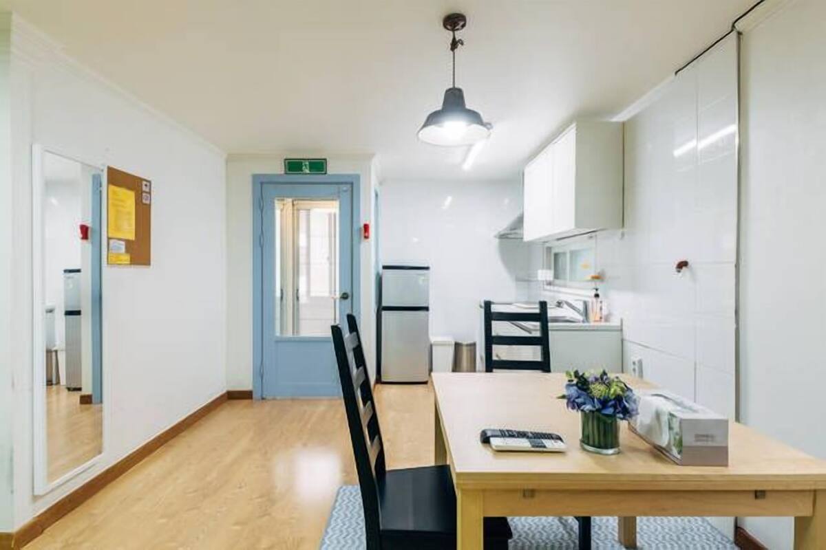 Une cuisine moderne avec une table à manger, des chaises, un réfrigérateur et un luminaire suspendu.