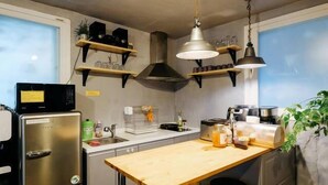Une cuisine compacte dotée d’un réfrigérateur en acier inoxydable, d’un plan de travail en bois, de luminaires suspendus et d’étagères intégrées.