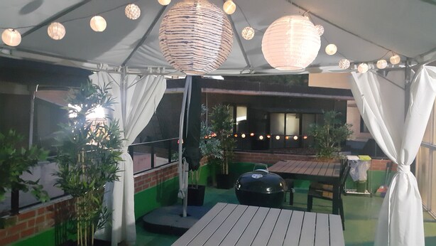 Un espace extérieur aménagé en patio, avec un coin salon couvert, des guirlandes lumineuses et des plantes en pot.