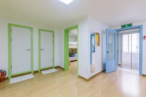 Un couloir avec trois portes, une bleue et deux vertes, qui donnent sur des chambres.