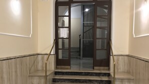 A set of marble stairs leading to a door with glass panels, flanked by walls with a marble base and a light-colored upper section. - Sweety (Rome)
