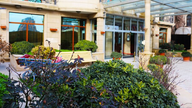 A hotel courtyard with a glass entrance, benches, and well-maintained greenery.