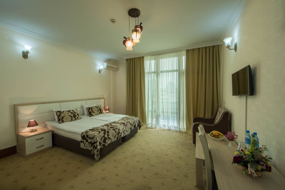 Une chambre d’hôtel comprenant un lit, une table de chevet, une lampe, une chaise et un bureau agrémenté d’un arrangement floral.