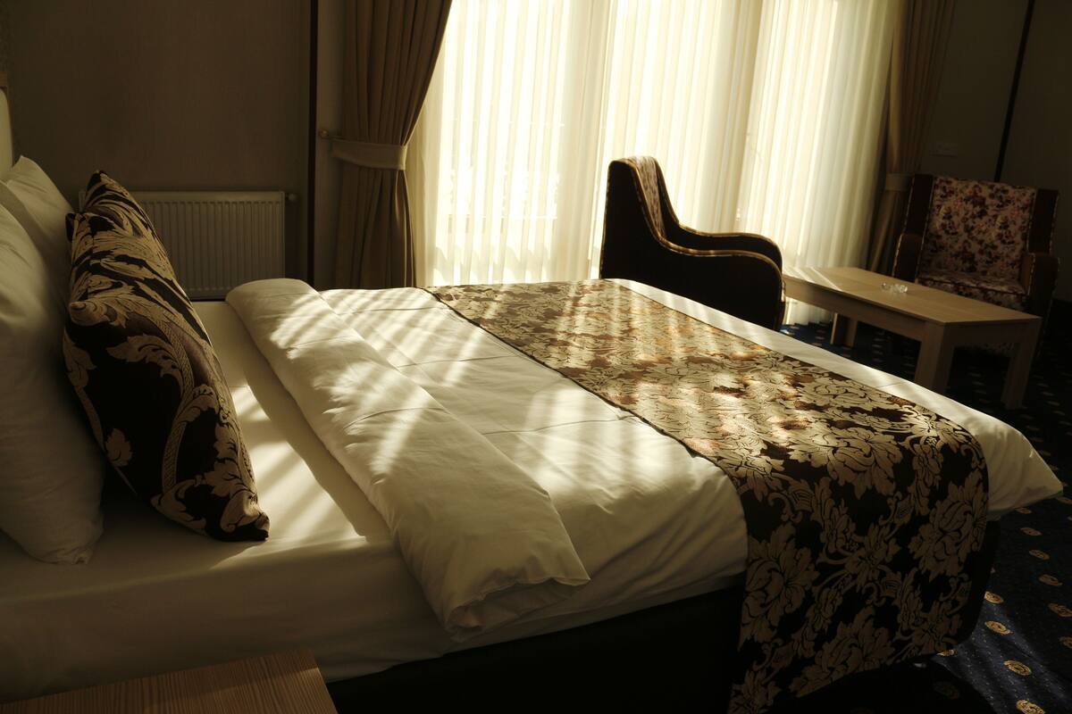 Une chambre d’hôtel avec un lit, une chaise, une table et une fenêtre avec des rideaux.