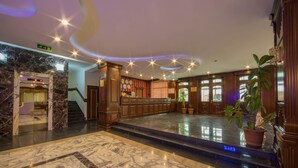 A lobby with marble flooring, wooden reception desk, and potted plants.