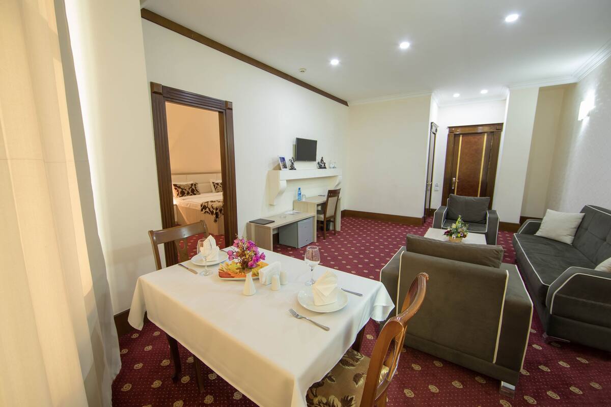 Un coin repas avec une table dressée pour deux personnes, un canapé et un petit espace salon avec un téléviseur.