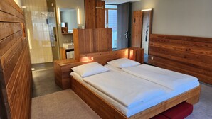 A wooden room with a bed, a wooden wardrobe, a mirror, and a bathroom with a shower. - Speidel's Brau Manufaktur (Hohenstein)