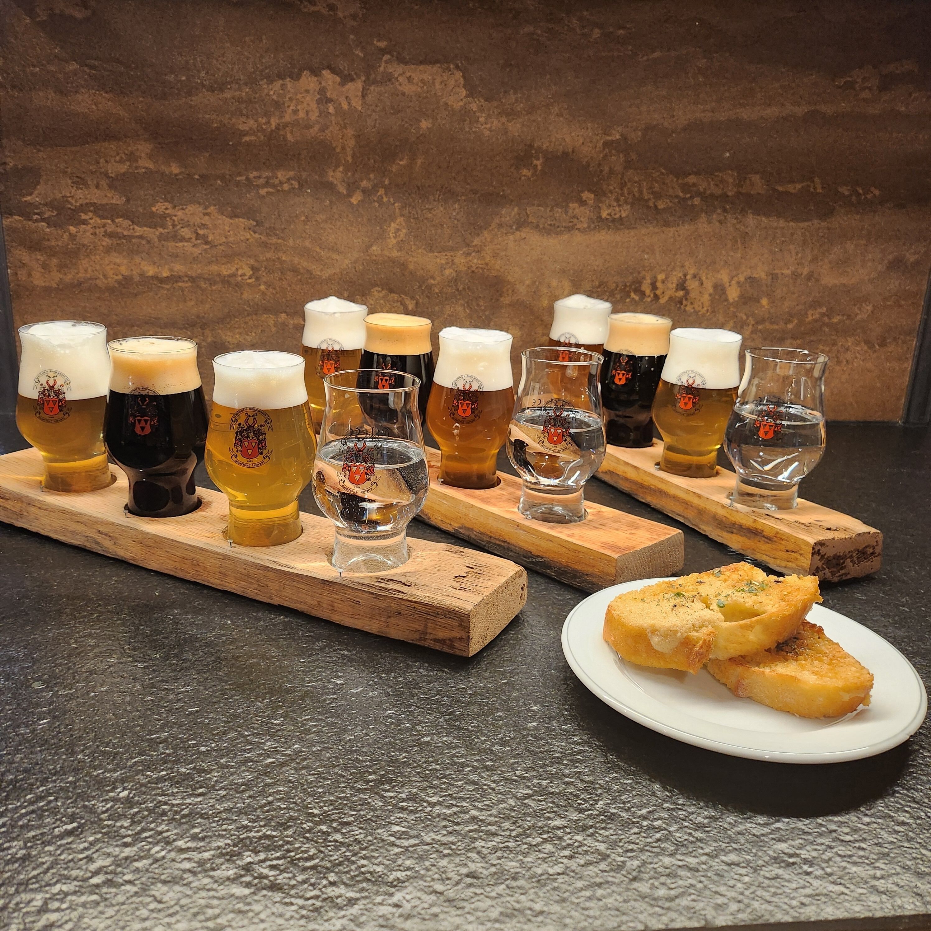 Verschiedene Biergläser auf Holztellern, im Vordergrund eine Platte mit Grissini.
