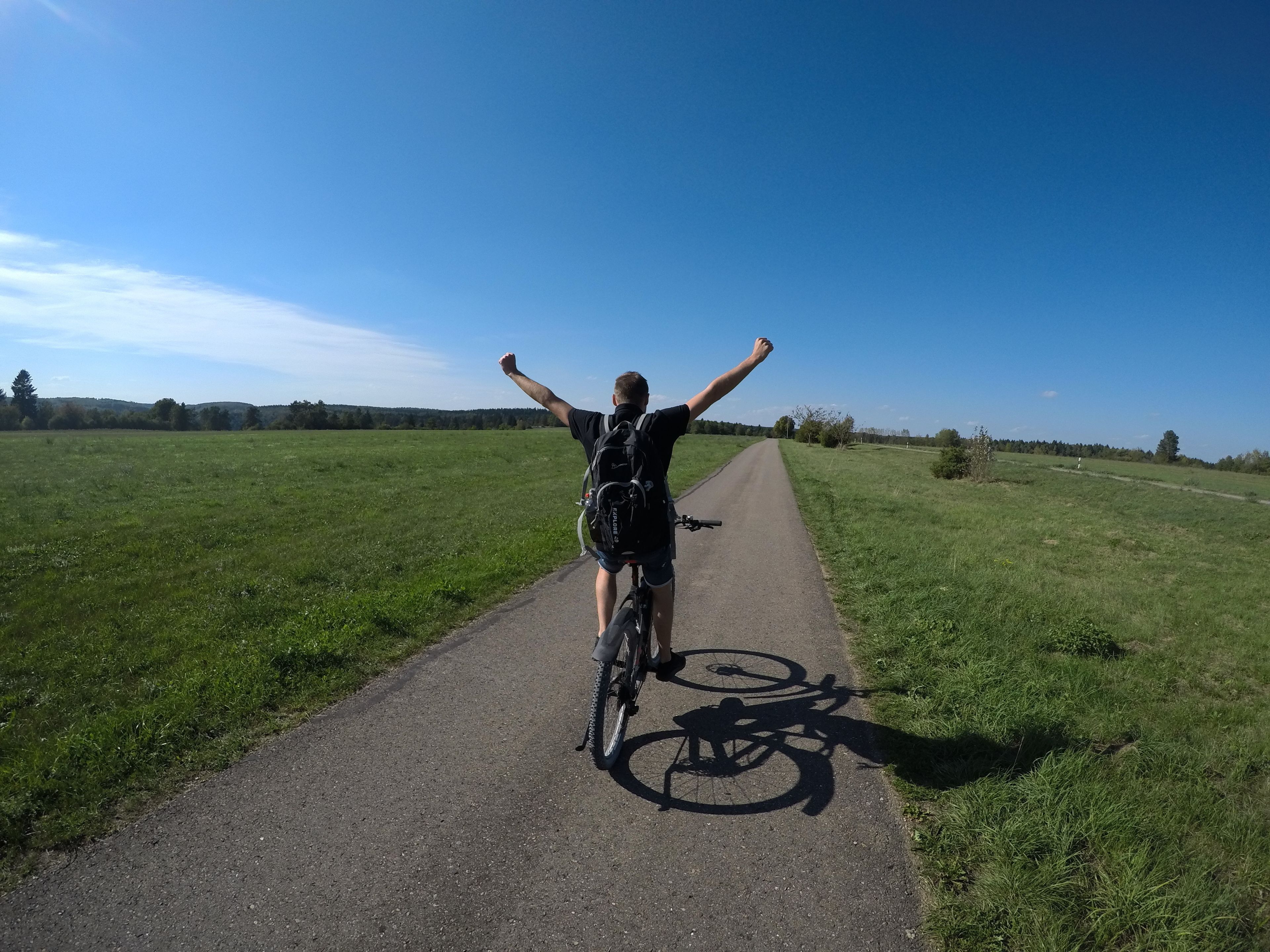 En person på en cykel som cyklar på en asfalterad stig med gräs på båda sidor.